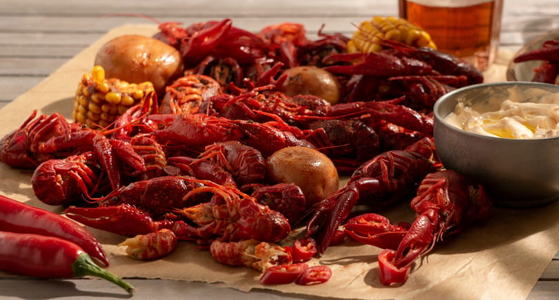 Boiled red crawfish, corn on the cob, potatoes, and chili peppers on brown paper.